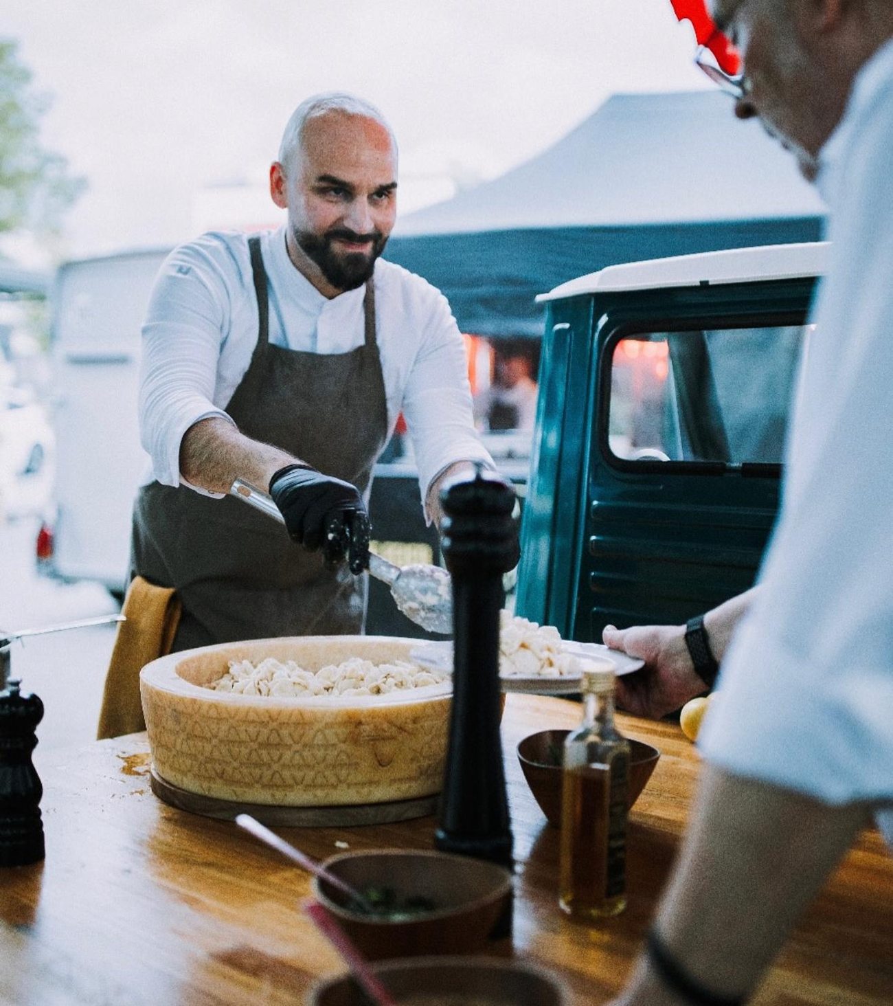 Stefano schöpft Pasta aus dem Parmigiano-Reggiano-Laib und reicht sie einem Gast, dahinter die Ape