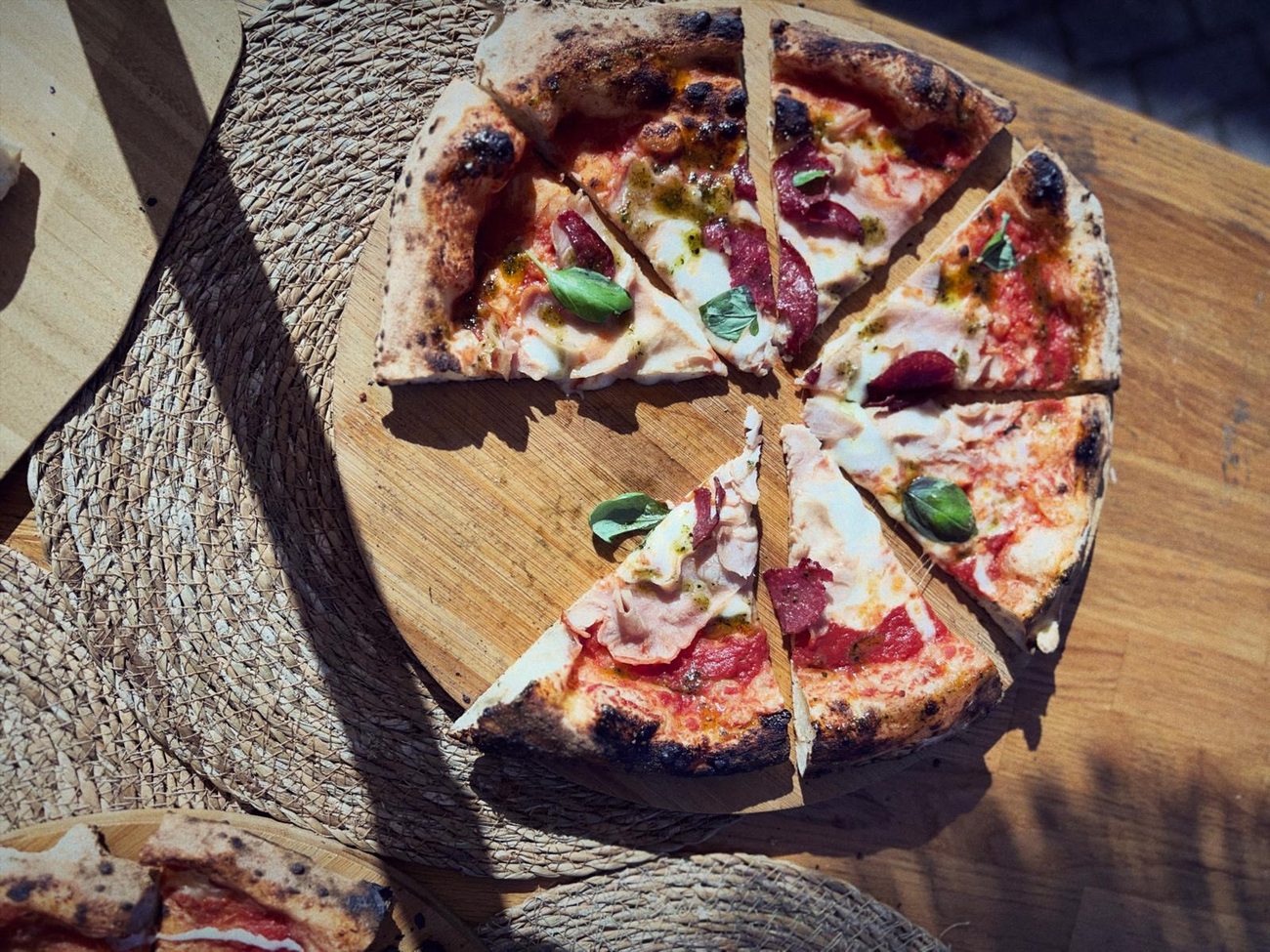 Aufgeschnittene Pizza auf einem Holzbrett in der Sonne