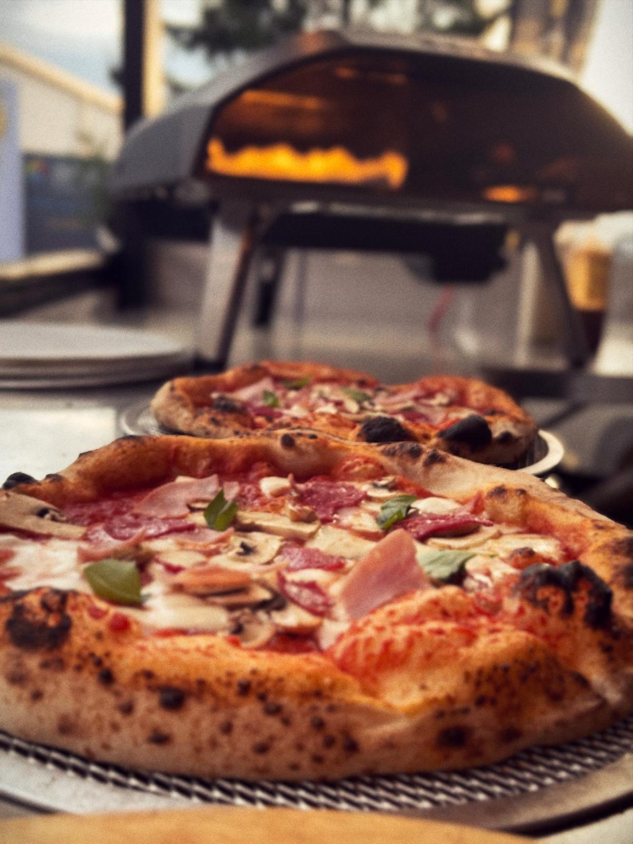 Zwei Pizzen vor dem Ofen, in dem die Flamme brennt
